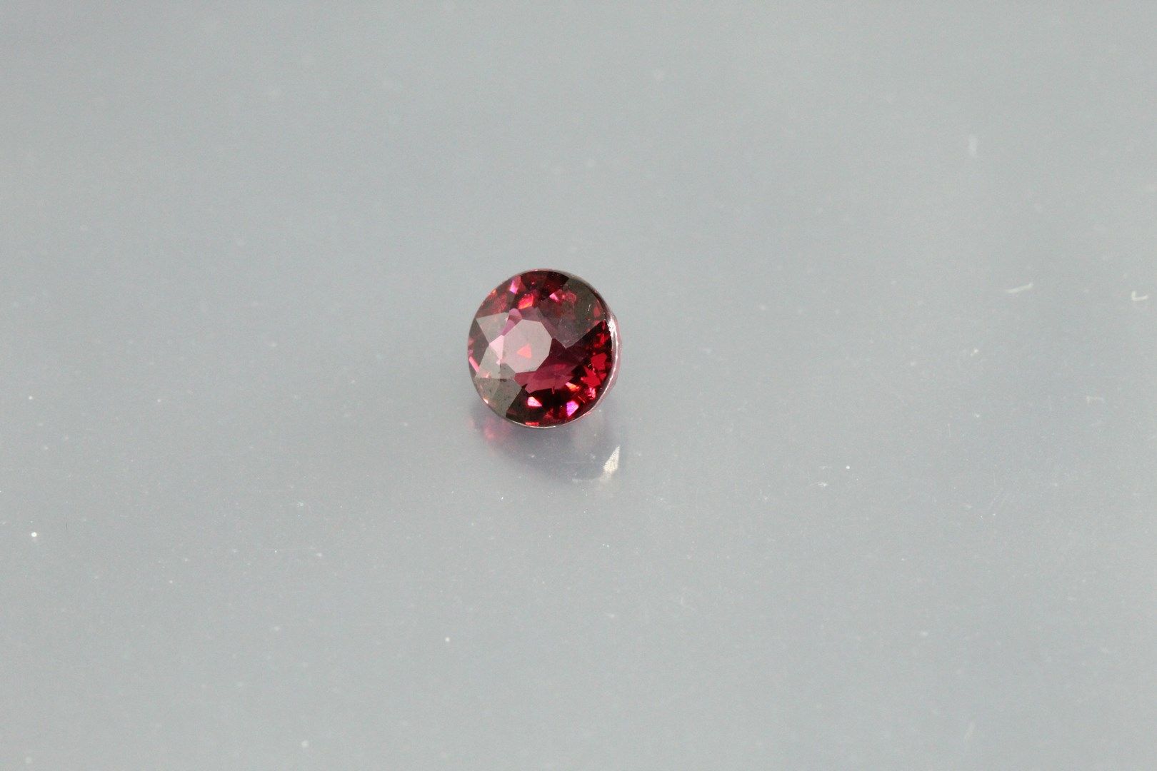 Null Rhodolite garnet (purplish red) round on paper.

Weight : 1, 09 cts.
