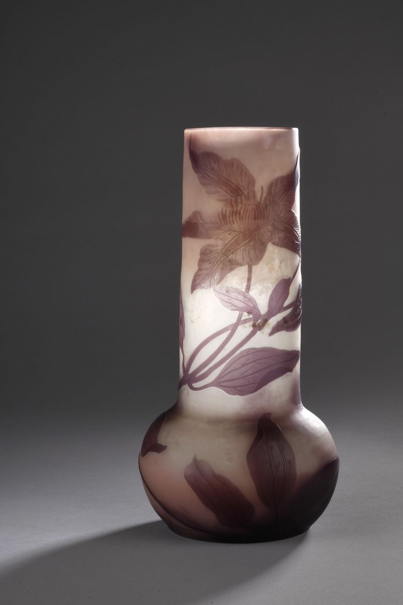 Null 加勒公司 
膨胀的底座上的管状花瓶。粉红色背景上的紫色内衬玻璃证明。浮雕雕刻的铁线莲。 
已签名。
高25,5厘米