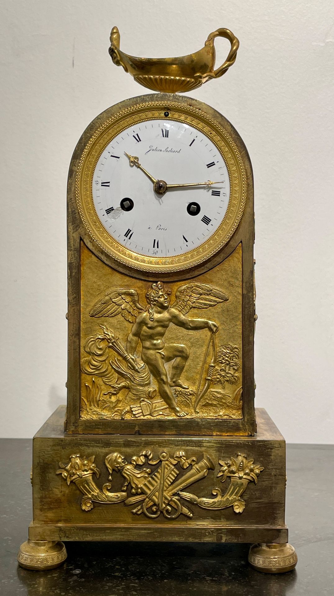 Null 一个装饰着爱情的木制和镂空铜钟。圆形珐琅表盘上有巴黎Julien Beliard的签名，顶部装饰着一盏油灯，它放置在四只耙脚上。帝国时期。高：34厘米&hellip;