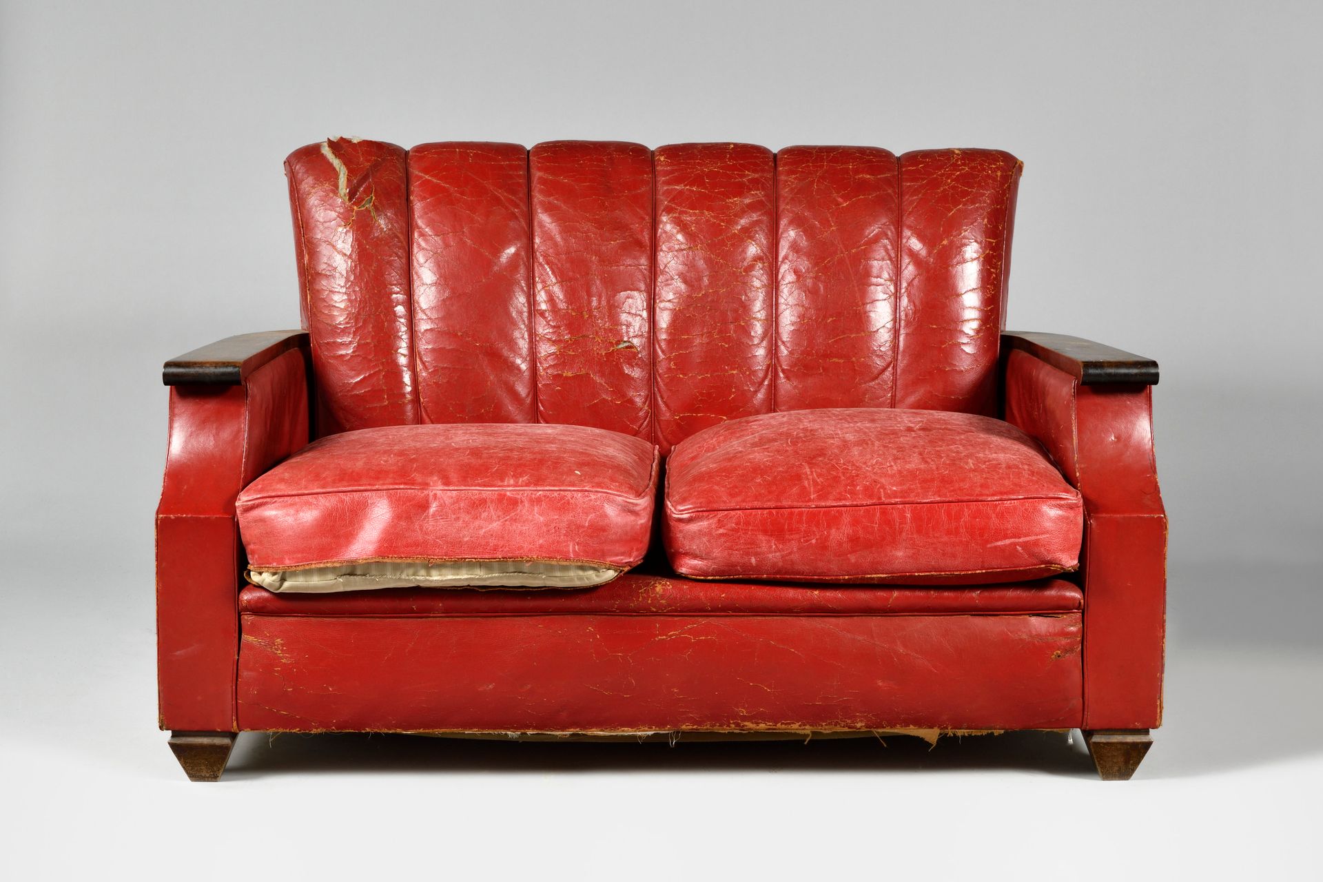Null JACQUES ADNET (1900-1984), 归属于一个红色的皮革沙发和一对扶手椅，清漆的木质扶手，弯曲的背部被滚边分割，站在金字塔形的腿上。&hellip;