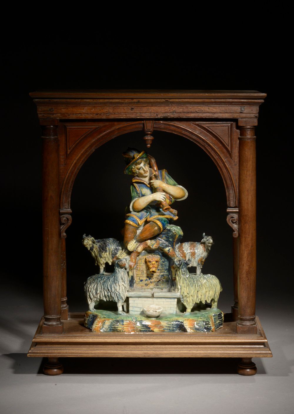 Null 小型多色珐琅彩陶器喷泉，表现一个牧羊人吹笛子，周围是他的羊群（事故和缺失）。

意大利，19世纪。

它以19世纪的锥形柱子和圆形拱门的胡桃木门廊呈现&hellip;