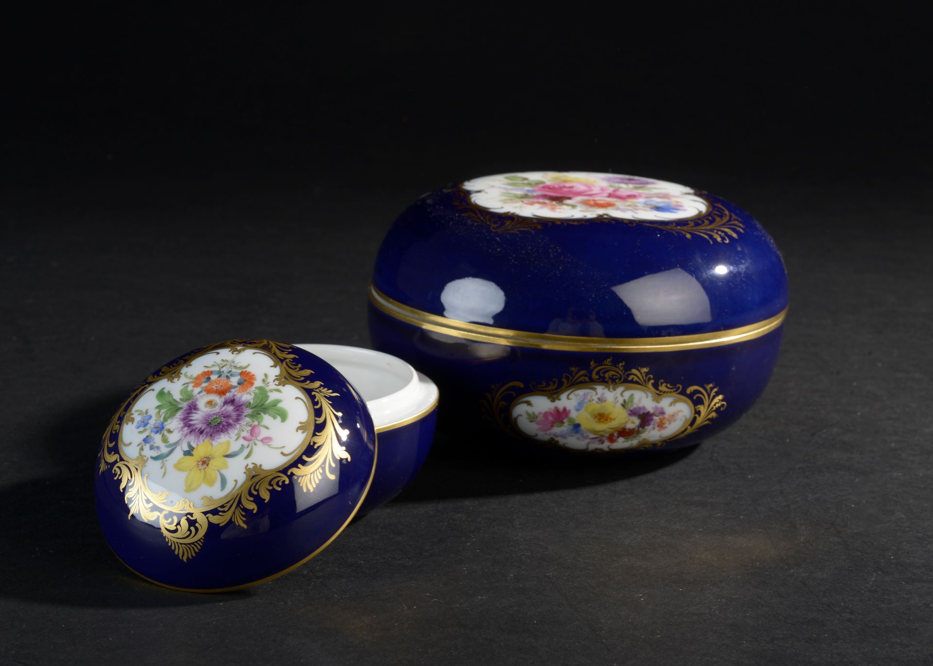 Null 迈森.
两个圆形的有盖瓷盒，蓝色背景上有花朵和镀金。
标记有交叉的剑。
20世纪。
直径：9和15.5厘米