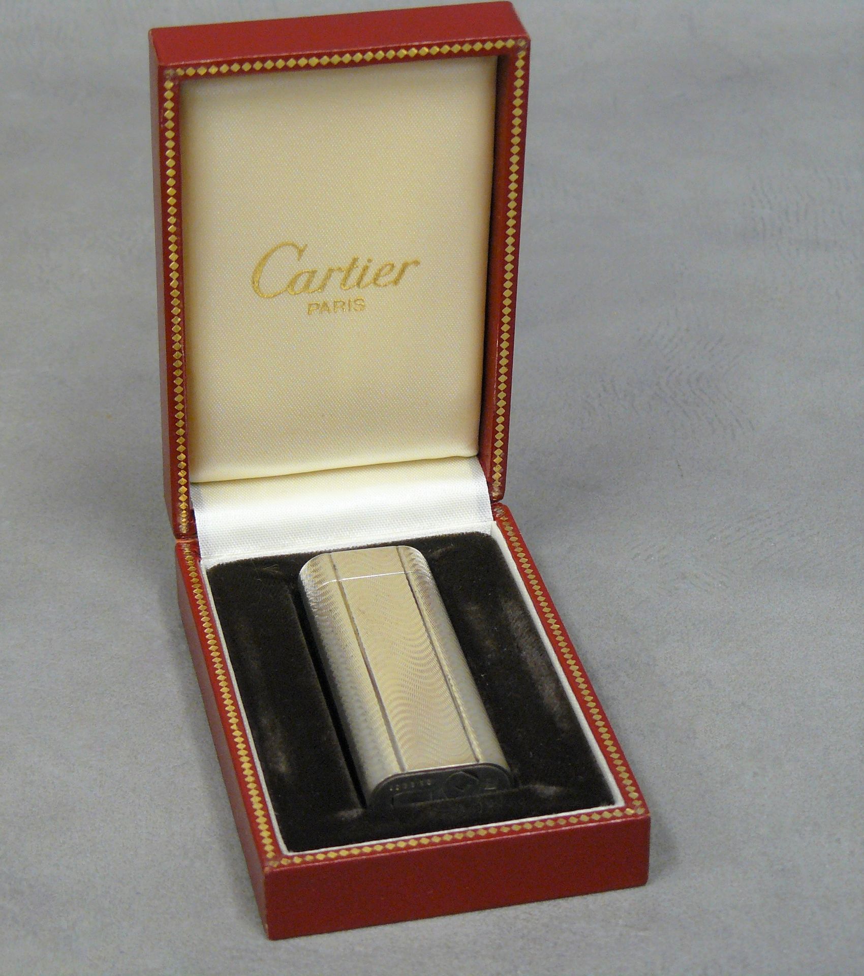 CARTIER CARTIER : un briquet plaqué argent à décor guilloché n° 052034 dans son &hellip;