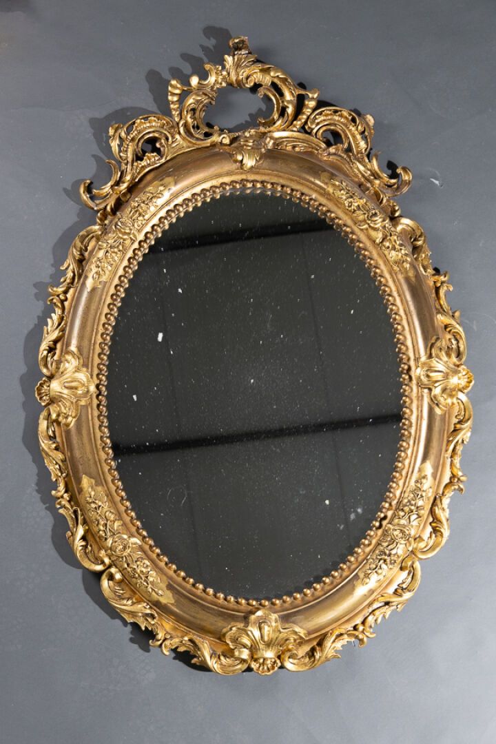 Null 椭圆形灰泥镀金木镜，饰有珍珠、玫瑰和碎贝壳（意外和缺失部分）楣饰。 
路易十五风格。 
镜高145 厘米 - 宽度：98 厘米