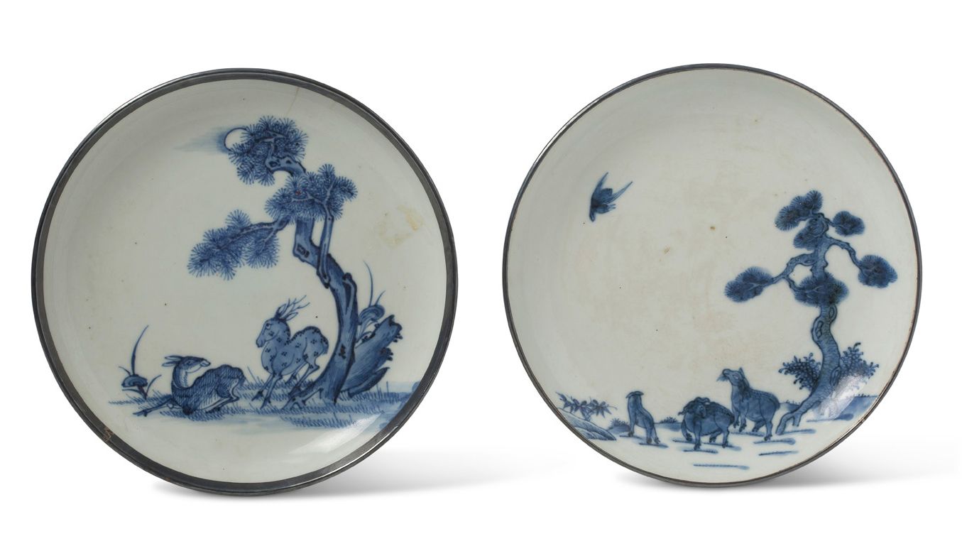 VIETNAM XIXe siècle 
两只青花瓷杯，一只装饰着松树下的一对鹿，另一只装饰着松树下的三只山羊，上部有一只鸟在潜水。每一个都有一个金属环形的边缘&hellip;