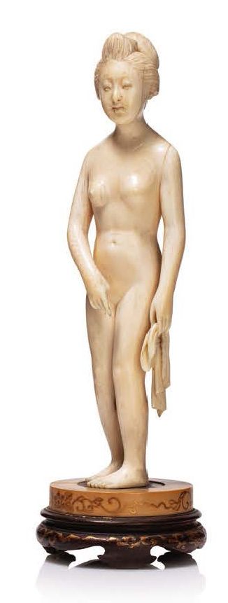 JAPON VERS 1920 象牙 Okimono 描绘了一个站立的裸体年轻女子，她拿着一块布，头发梳成发髻。
安装在一个双底座上，由深色和浅色的木头制成，装&hellip;