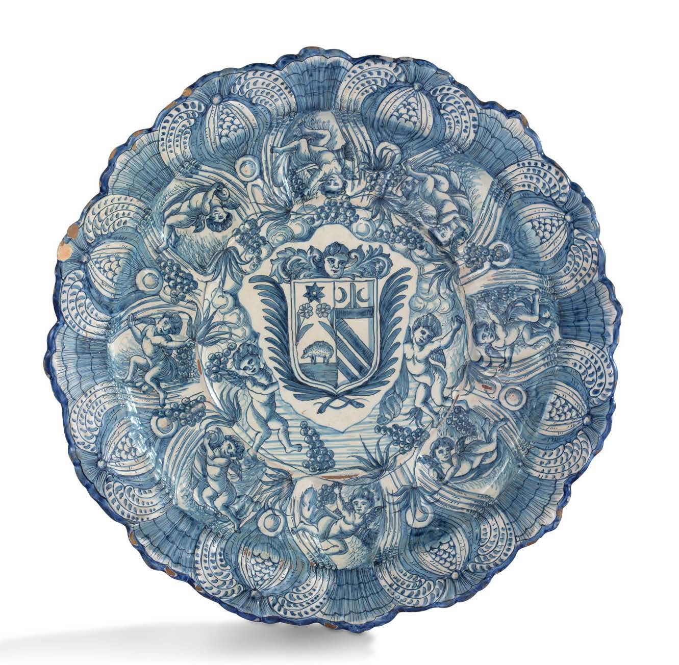 SAVONE 一个大的圆形陶器盘子，中间用蓝色单色装饰着纹章和一个带翅膀的孩子的爱，框架中的叶子在浅浮雕中形成一个花环。标记。意大利，可能是萨沃纳，18世纪（？&hellip;