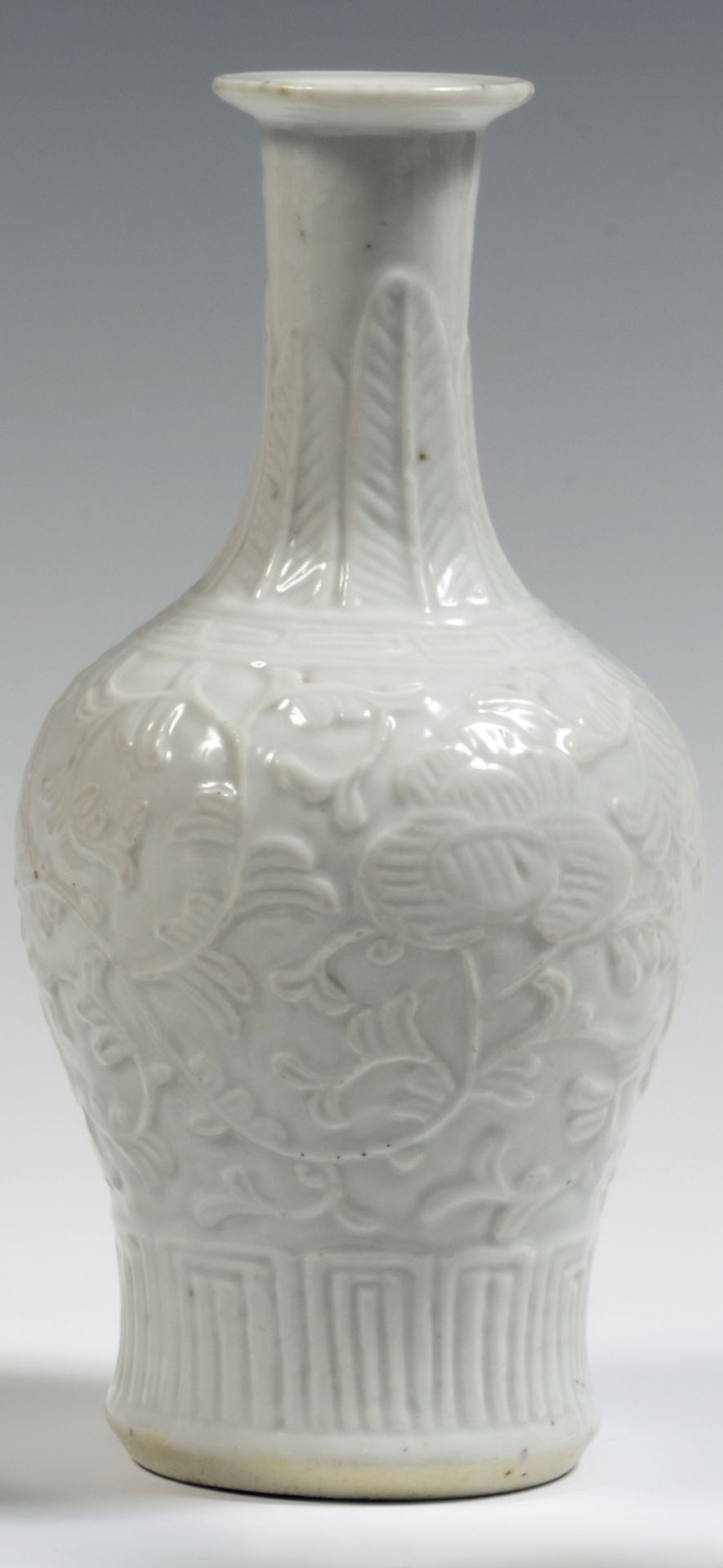 Null 
中国

一个白瓷柱形花瓶，颈部有荷花、叶子、几何图案和香蕉叶的浮雕装饰。

19世纪。 

H.23厘米。

颈部有一个小缺口。