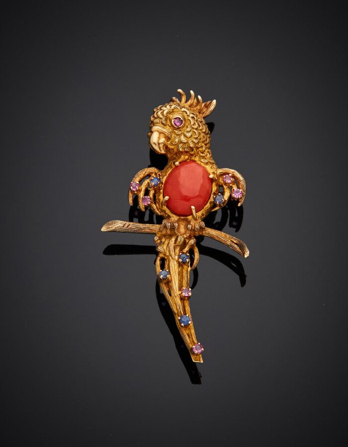 Null 黄金（750）"鹦鹉 "胸针，雕刻并以椭圆形珊瑚凸圆形为中心，镶嵌小红宝石和蓝宝石。白金（750）针。约1960年。

长度：5厘米。毛重：10克。