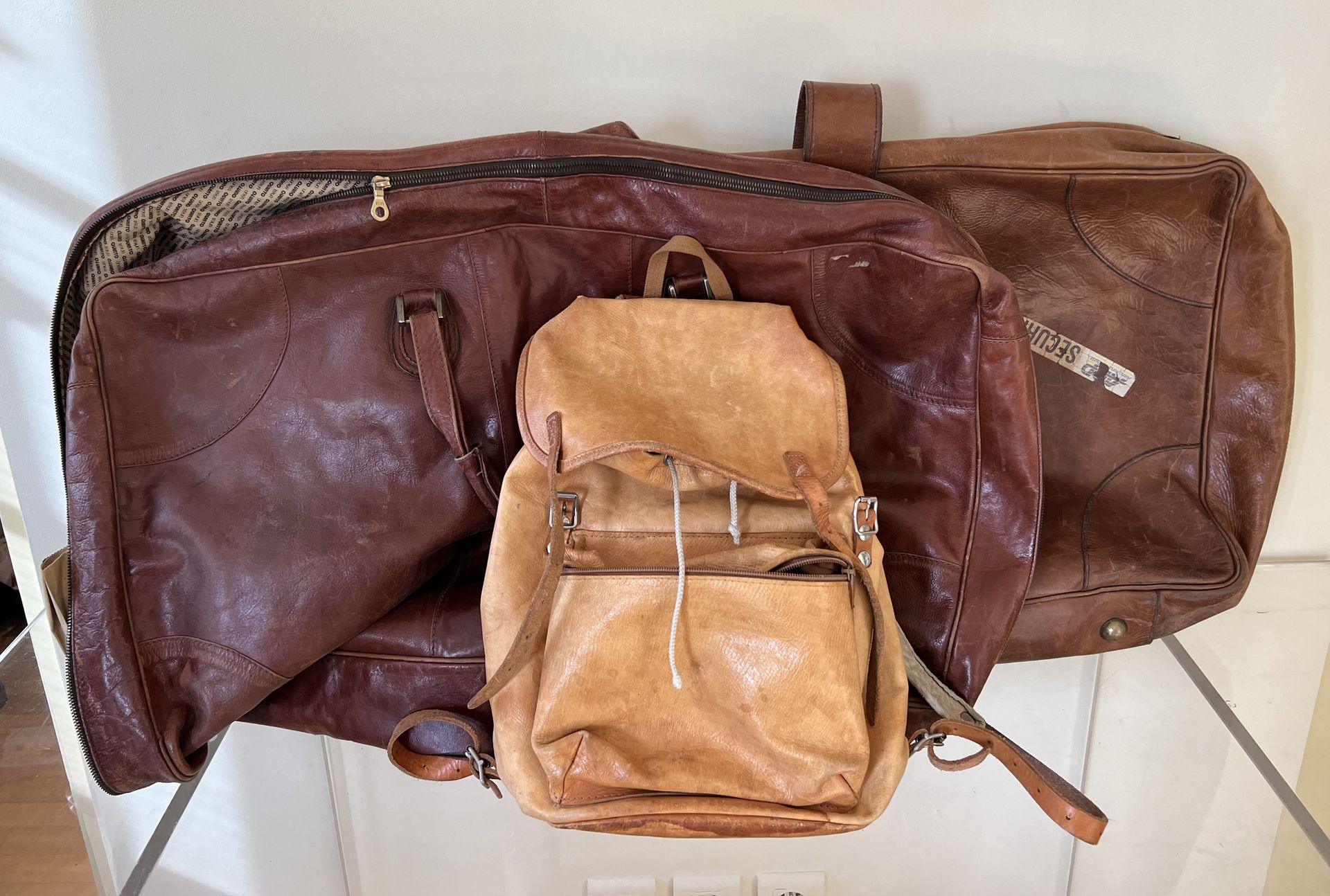 Null Two leather travel bags in used condition. A leather backpack is included.