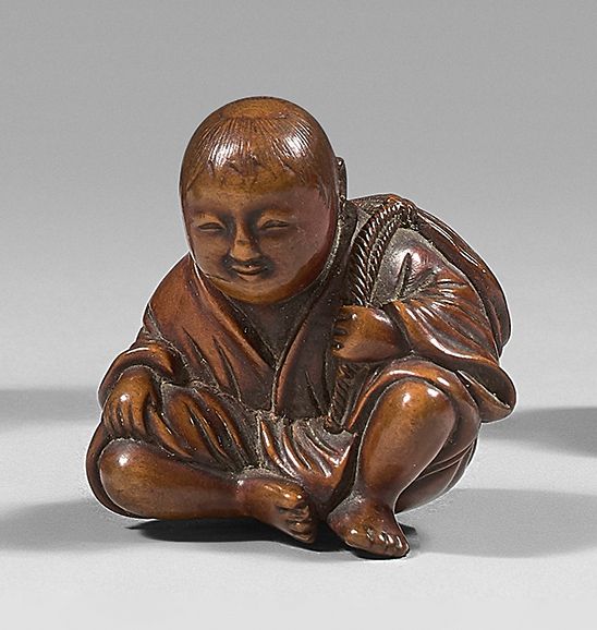 JAPON - Époque Edo (1603-1868), XIXe siècle Netsuke en buis, enfant assis, porta&hellip;