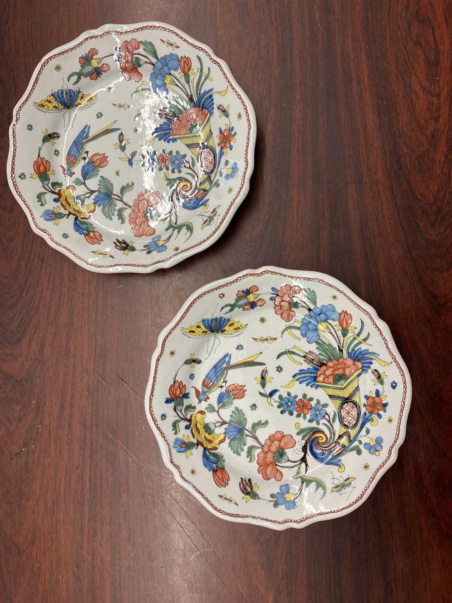 Null ROUEN一对陶制盘子，有一个轮廓的边框，上面有多色的装饰，有康乃馨和蝴蝶从里面飞出来的角，一只凤凰栖息在花枝上。 18世纪。 D : 25 cm