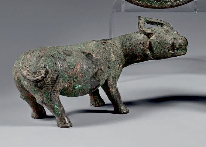 CHINE - Style Archaïque 一尊绿色铜锈的水牛雕像，站立着，头转向右边，侧面的毛被凿开。
(已氧化)。
高：10.5 - 长：20厘米