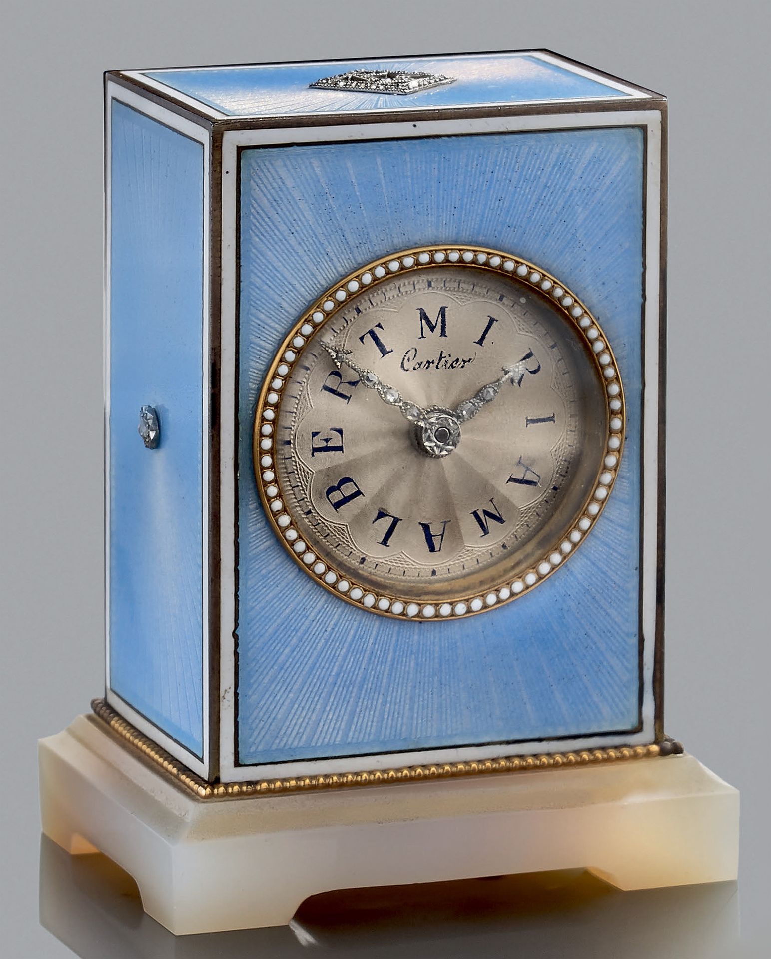 CARTIER 800千分之一的镀金旅行钟，在放射状的玑镂背景上涂有半透明的蓝色珐琅，并以白色珐琅网加强。它放置在一个玛瑙底座上。银色表盘上绘有阿拉伯数字 "A&hellip;