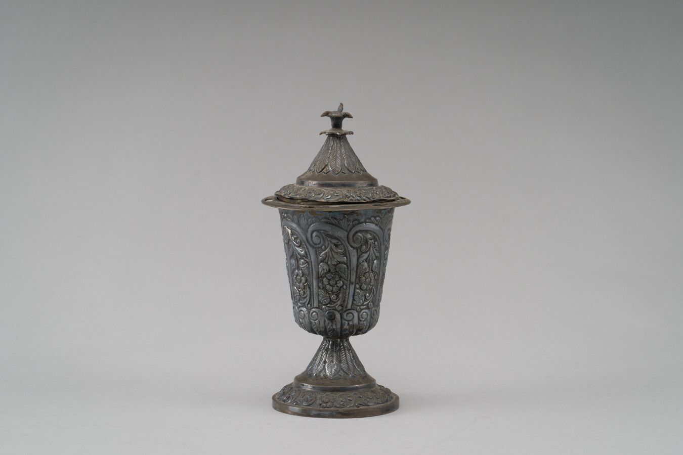 Null 银质糖碗，上面压印有卷轴式的花枝装饰。底座上有羽毛和花纹的衬托。

盖子的形状是一只鸟。

可能是19世纪的奥斯曼作品。

(许多凹痕)

重量：31&hellip;