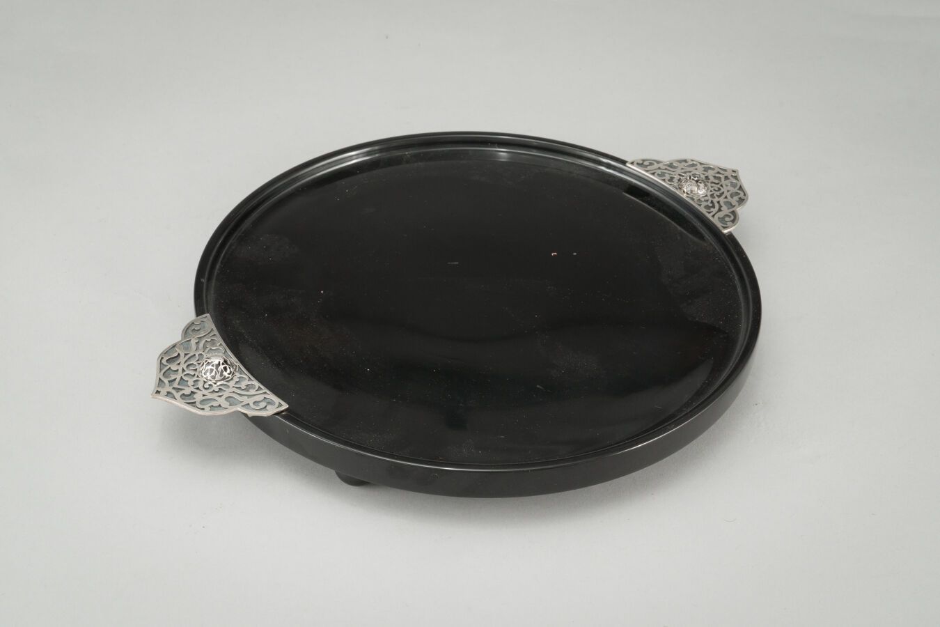 Null ARMAGGAN:

棕黑色有色玻璃或树脂的圆形服务盘，手柄为镀银金属，有镂空装饰。

签名。

(小的凹痕)。

直径：29厘米。

长：36.5厘&hellip;