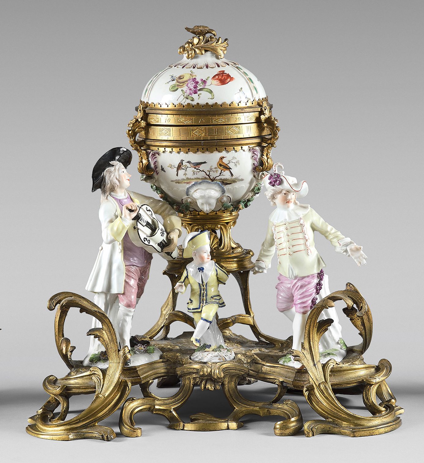 Null 鎏金铜质双表盘时钟，装饰有三个迈森瓷器雕像。镂空的罗盖尔底座。
部分是18世纪的。
 （综合，非常小的事故）。
高度 : 37 cm - 宽度 : 3&hellip;