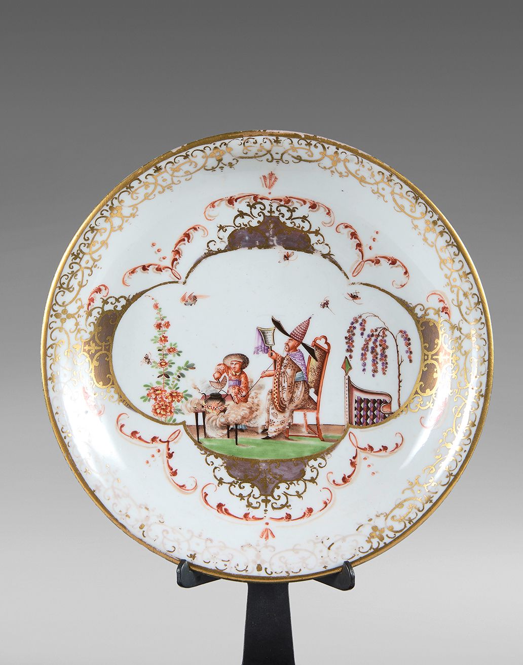 MEISSEN 一个圆瓷碗，有多色和金色的装饰，中央有两个中国人坐着，鸟和昆虫，边缘有叶子、花边和楣饰。
大约1725-1730年。
直径：17厘米