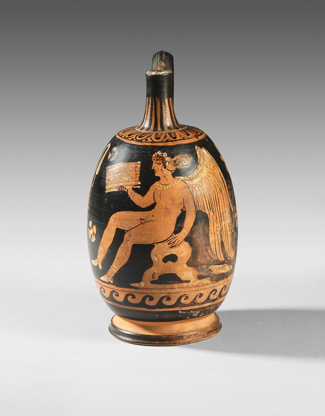 Null 红色图案的Aryballisque lekythos，代表一个坐在岩石上的雌雄同体的Eros，手持一个盒子。 
粘土，白色油漆突出。
缺少颈部。
希腊&hellip;