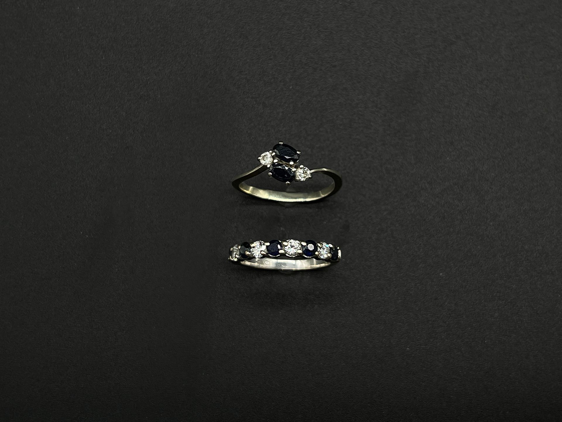 Null 两枚18K(750千分之一)白金戒指，包括一枚半环镶嵌明亮式切割钻石与圆形刻面蓝宝石交替的戒指和一枚镶嵌两颗椭圆形蓝宝石、边缘镶有两颗小钻石的戒指。
&hellip;