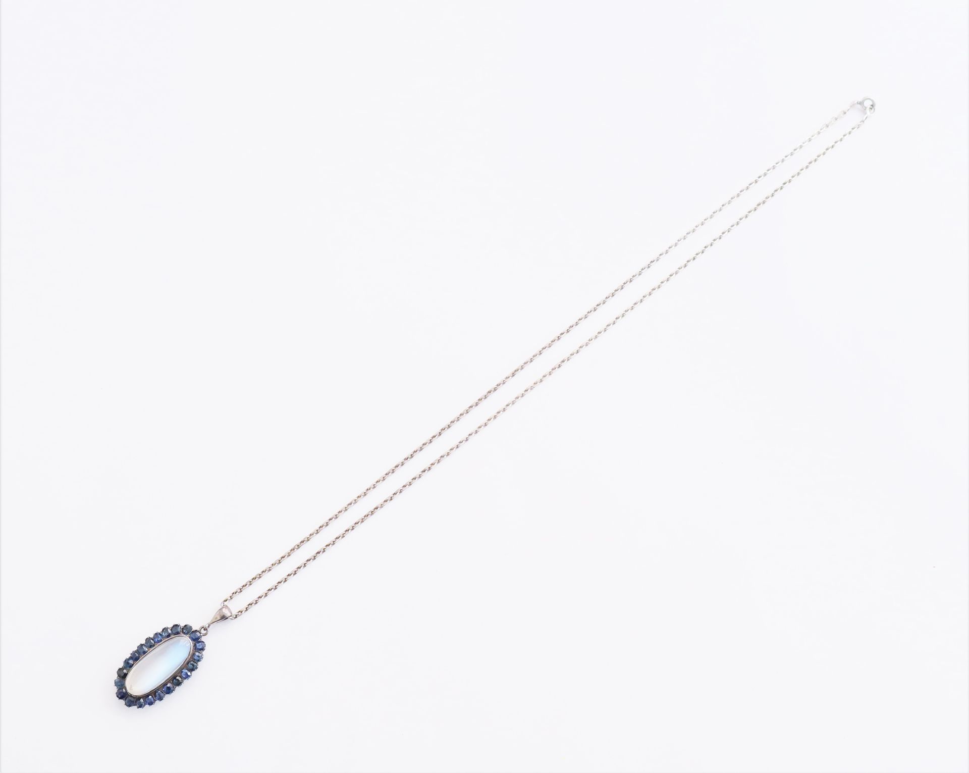 Null 银质吊坠上镶嵌着椭圆形凸圆形月光石，周围环绕着蓝宝石，滑动在银质链条上。法国的工作。尺寸：3.3 x 1.5厘米左右。毛重 : 14,1 g