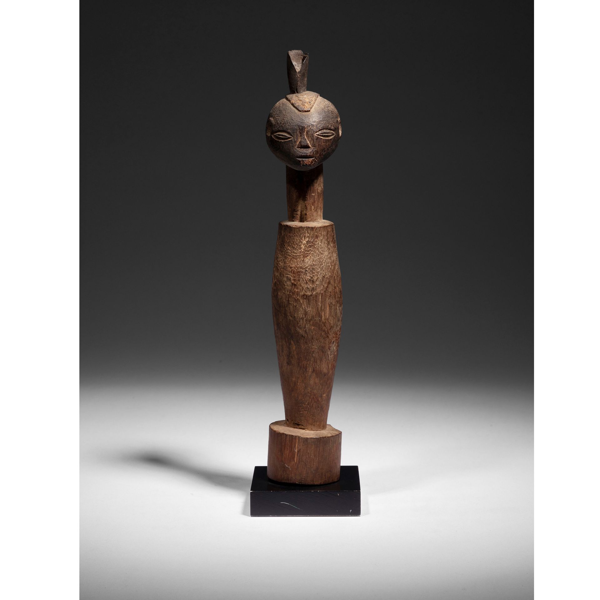 Null An old statuette carved in an oblong spindle on a cylindrical base surmount&hellip;