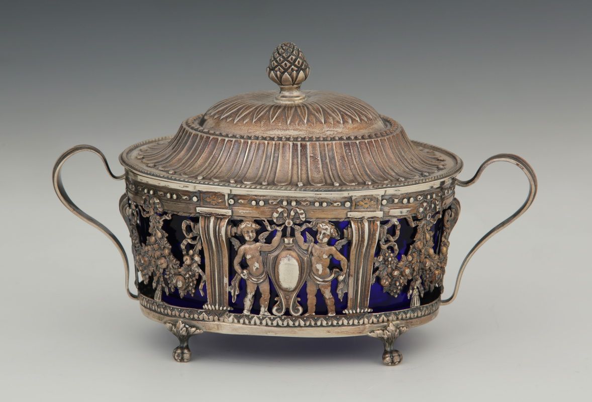 Null 一个路易十六风格的椭圆形有盖糖碗，带有Minerva 950 Millièmes银质支架，大约在1900年，上面有镂空和重塑装饰的爱情，拿着护身符和花&hellip;