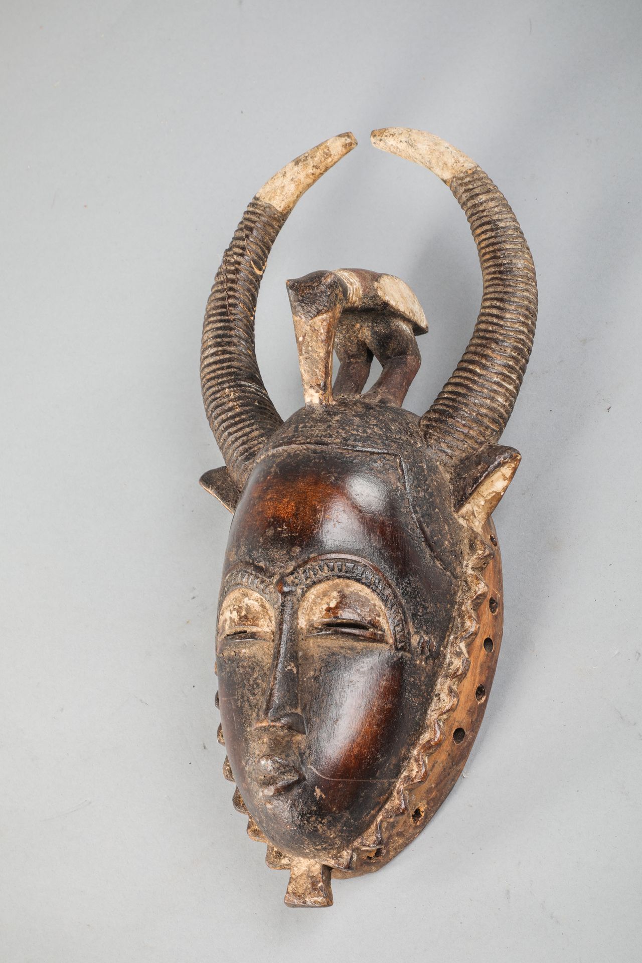 Null 象牙海岸的Yaoure面具，显示了一个逼真的面部造型，上面有一对角和一只角鸟。木头，黑褐色铜锈，高岭土。高42厘米。