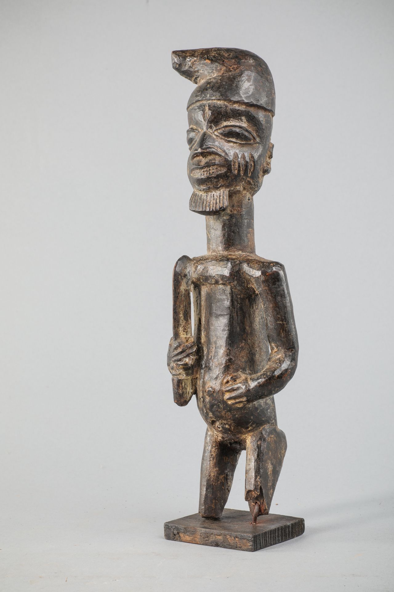 Null 约鲁巴雕像，尼日利亚，一个戴着帽子和剑的男性贵宾，一只手放在脐部。硬木，有旧的黑褐色斑纹，缺失。高37厘米。