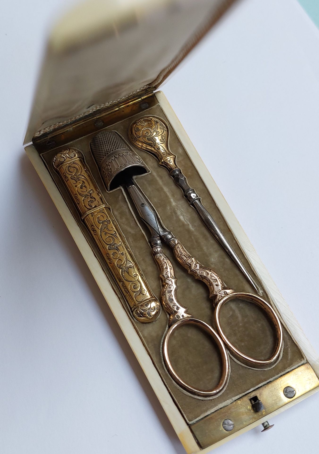 Null 鎏金和钢制的服装用品，包括一个针盒，一把剪刀和一个花边针，刻有叶子，放在一个象牙盒子里，19世纪末的作品。

毛重29克