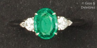 null White gold ring set with a faceted oval emerald set with heart-cut diamonds....