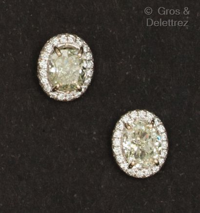 null A pair of white gold earrings set with an oval-cut diamond in a circle of brilliant-cut...