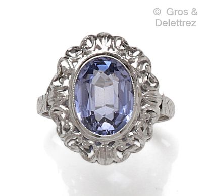 null Bague en or gris, ornée d’une pierre bleue dans un entourage de volutes ajourées....