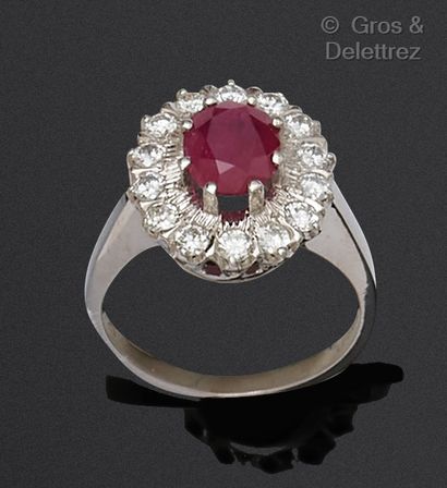 A white gold ring set with an oval ruby in...