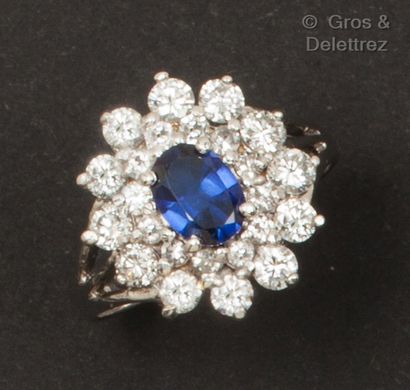 null A 14K white gold ring set with an oval sapphire in a double border of brilliant-cut...