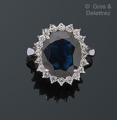 null White gold ring set with an oval faceted sapphire in a brilliant-cut diamond...