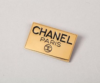 CHANEL Broche plaque en métal doré ré haussé de l'écriture Chanel émaillé noir.