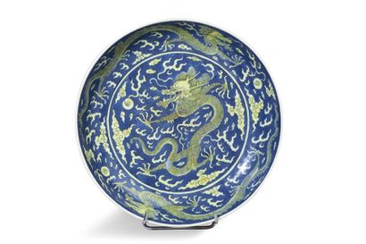 null Plat creux en porcelaine émaillée bleu et jaune à décor de trois dragons pourchassant...