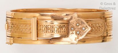 null Bracelet rigide ouvrant en or jaune ciselé à décor d’une boucle sertie de demi-perles....