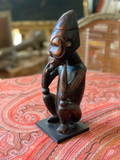null Statuette africaine en bois sculpté représentant un personnage accroupi se tenant...