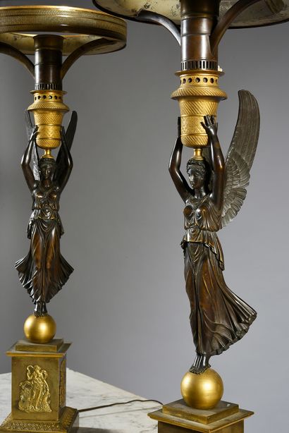 null A pair of lamps in patinated and gilt bronze, formed by a winged victory supporting...