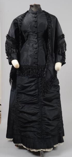 null Robe vers 1885, en taffetas de soie noir, garnie de franges de rubans de même...