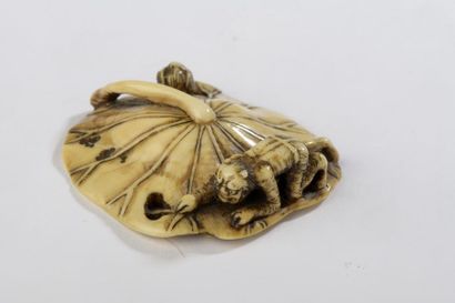 null Netsuke en ivoire à patine jaune, oni attrapant un namasu sous une feuille de...