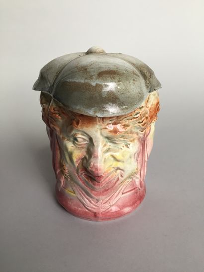 null A tobacco jar with three characteristic faces, wearing a peaked cap. 

Glazed...