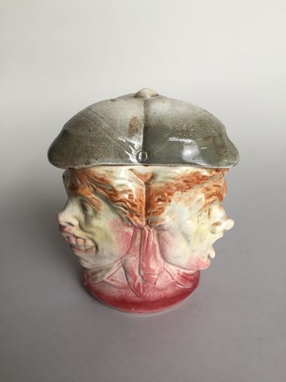 null A tobacco jar with three characteristic faces, wearing a peaked cap. 

Glazed...