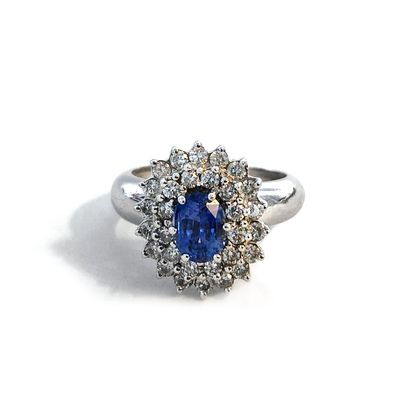 null An 18K white gold ring centered on an oval blue sapphire surrounded by round...