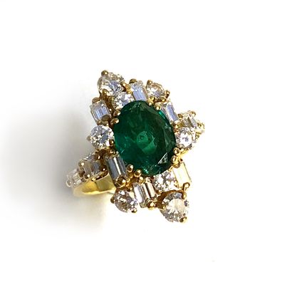 null An 18K yellow gold ring centered on an emerald surrounded by round and baguette-cut...