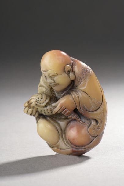 null CHINE - Vers 1900.
Statuette de Luohan assis en stéatite beige et rouge tenant...