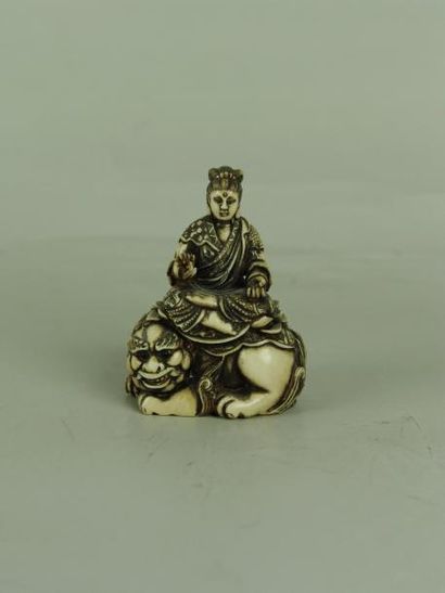 null NETSUKE EN IVOIRE. Représentant une Kannon assise sur un lion. (Signature dans...