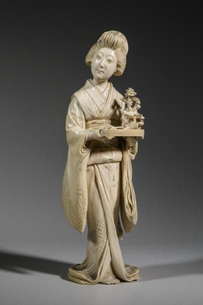 null Okimono en ivoire sculpté représentant une geisha portant un plateau.
Japon,...